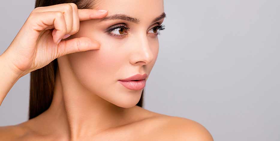 Closeup profile photo of lady pointing to eyebrow and under eye area with naturally arched eyebrow