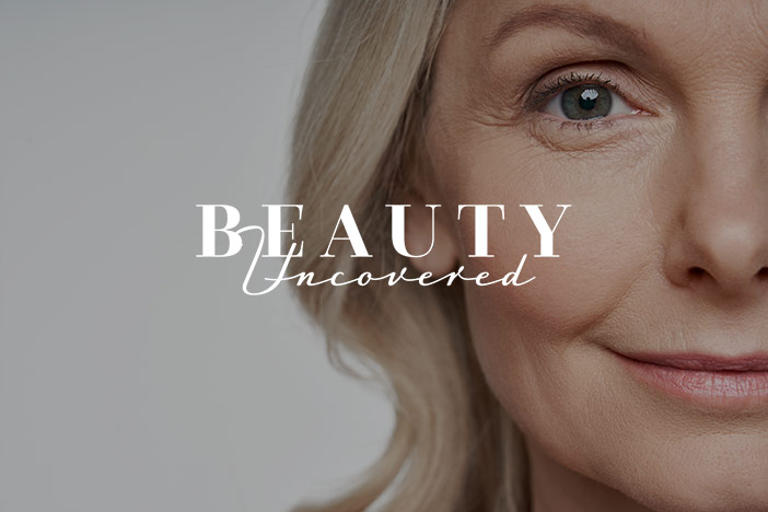 An older woman with wrinkles around the eyes and face looks at the camera with the Beauty Uncovered logo superimposed on top