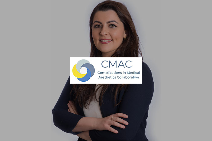 Miss Elizabeth Hawkes stands smiling with folded arms. The 'CMAC-UK' logo is superimposed on top. 