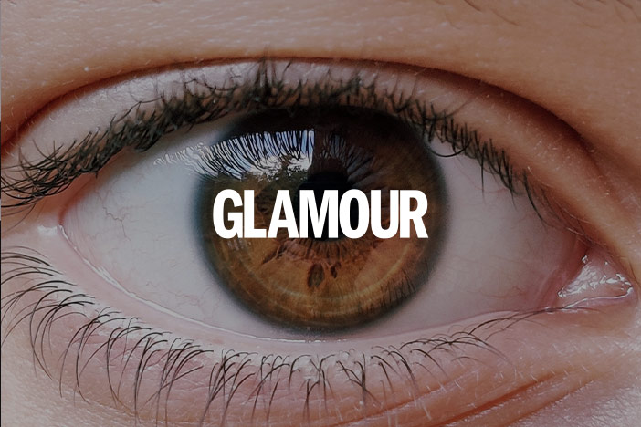 A brown eye belonging to a female with naturally long, thick eyelashes looks into the camera. A 'Glamour' Magazine logo is superimposed on top.