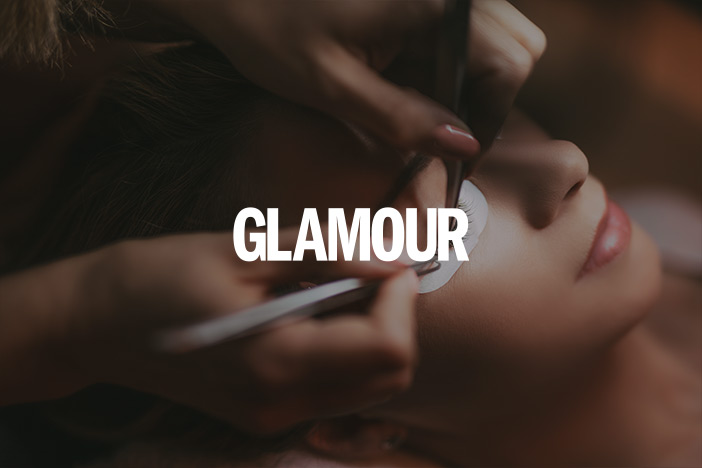 A middle aged woman is having her eyelash extensions done. A 'Glamour Magazine' logo is superimposed on top.