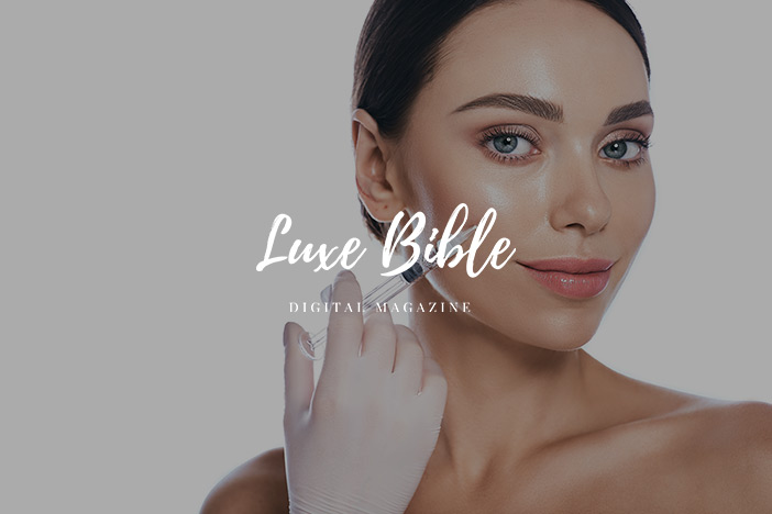 A younger woman receives a dermal filler injection to the cheek with the Luxe Bible logo superimposed on top