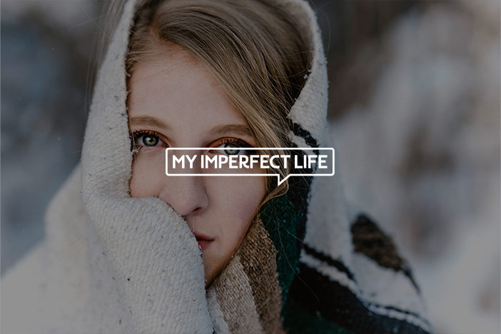 A middle ages woman outside in winter wrapped in a cosy blanket stares into the camera with the My Imperfect Life logo superimposed on top