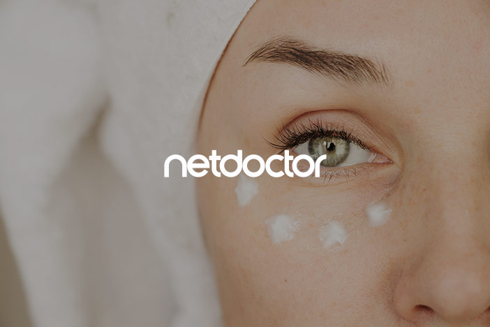 A woman with no visible dark circles under the eye and dots of eye cream spread across her under eye looks into the camera. A 'Net Doctor' logo is superimposed on top.