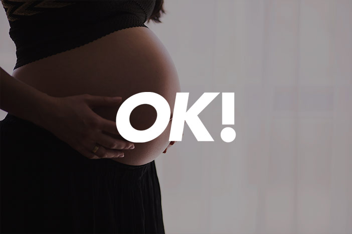 Pregnant woman holds bare pregnant belly. 'OK' Magazine logo is superimposed on top. 
