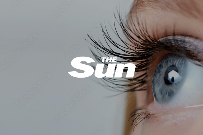 A blue female eye with long eyelashes, looking upwards. The Sun logo is superimposed on top.