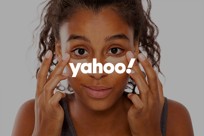 A dark skinned woman applies cream under the eyes in order to hide dark circles with the Yahoo! logo superimposed on top