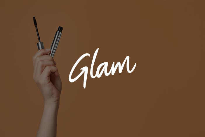 Hand holding mascara wand with Glam logo in white font on a brown background