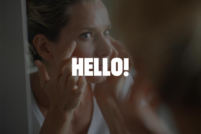 Woman applying skincare while looking in the mirror, featuring the 'HELLO!' logo.