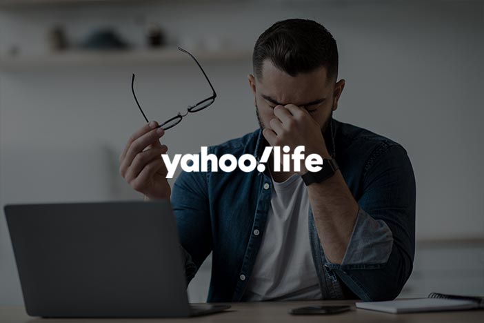 Yahoo Life explores screen time and eye dryness in adults Man sitting at a desk with eyes closed, holding glasses, appearing fatigued, rubbing dry eyes